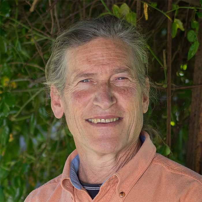 David Holmgren, co-originator of permaculture, smiling outdoors against green foliage.