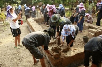 Workshop participants building up an earthen wall course by hand from wet mud and bricks while others watch and photograph, at Earth Home Thailand (Maejo Baandin), Mae Taeng, Chiang Mai.