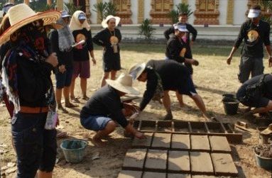 A group of people in sun hats laying out freshly moulded mud bricks on the ground to dry during a natural-building workshop, at Earth Home Thailand (Maejo Baandin), Mae Taeng, Chiang Mai.