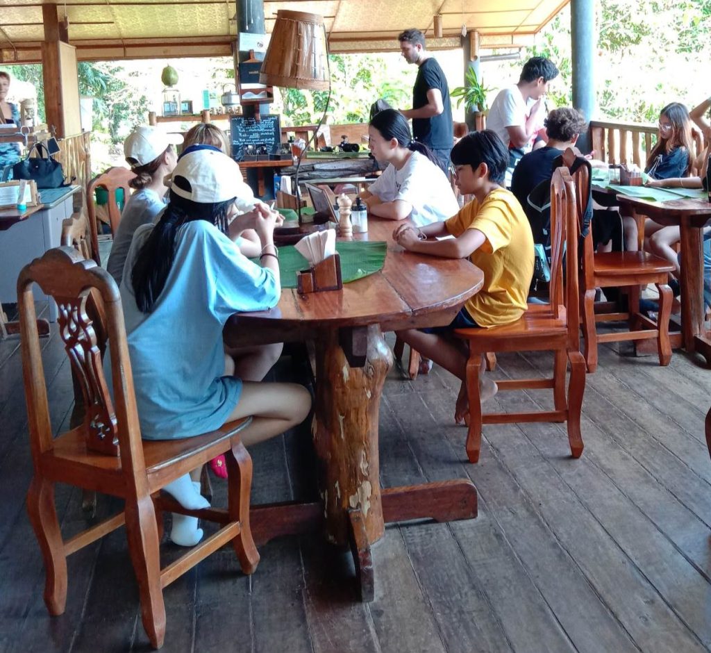Guests seated at rustic wooden tables in the open-sided Slow Food restaurant at Eco-Logic Thailand, Phato, Chumphon.