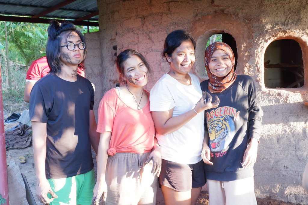 A group of course participants standing together and smiling in front of a brick natural-built structure at Gaia Ashram.