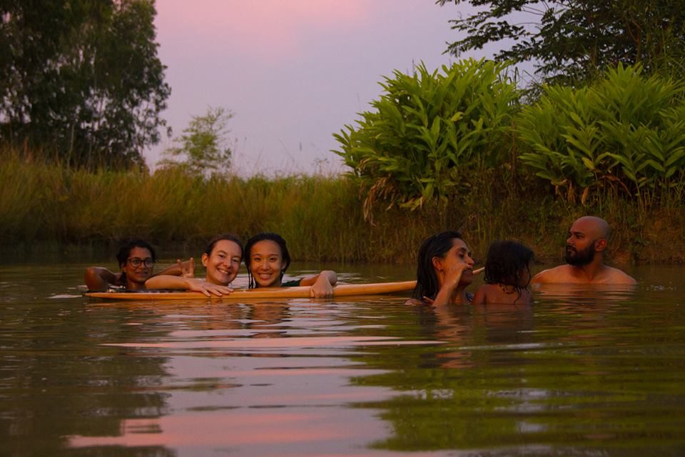 People cooling off together in a natural pond at sunset, surrounded by greenery, at Gaia Ashram.