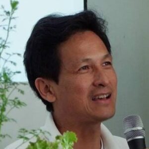 Komson Hutapaed, urban-farming pioneer, smiling and speaking into a microphone beside leafy green vegetables.