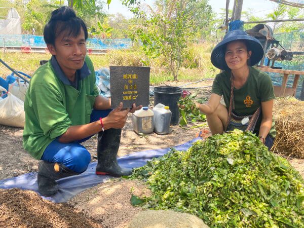 Two people mixing organic compost materials in a basin at Suan Na Ta Bua, demonstrating the farm's composting method.