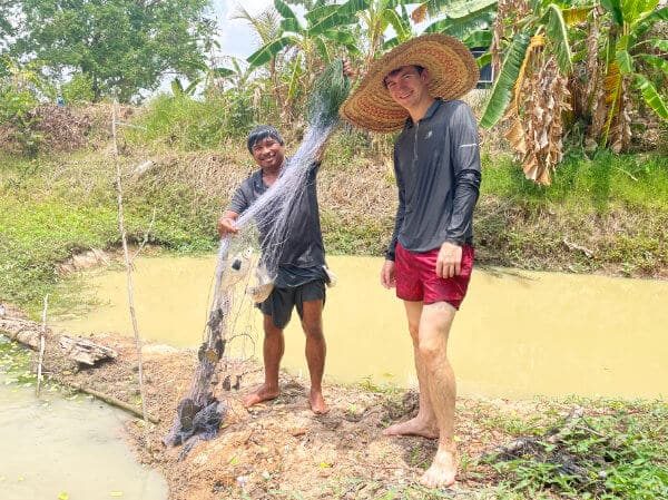 A visitor fishing at the edge of one of the farm ponds at Suan Na Ta Bua organic farmstay in Ubon Ratchathani.