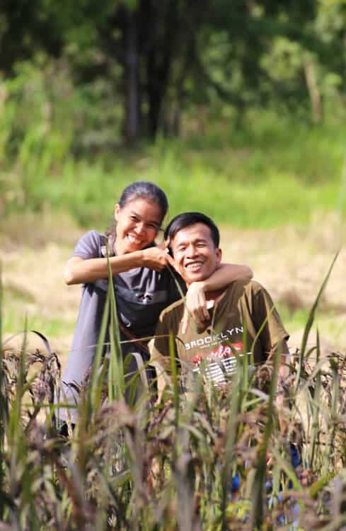 P'Rung and P'Kek, the husband-and-wife hosts of Suan Na Ta Bua organic farmstay, smiling together in their rice field in Ubon Ratchathani.
