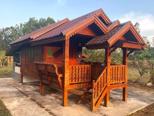 The wooden guest homestay at Suan Na Ta Bua, a raised traditional Thai cabin with a terrace and steps, set on the organic farm in Ubon Ratchathani.