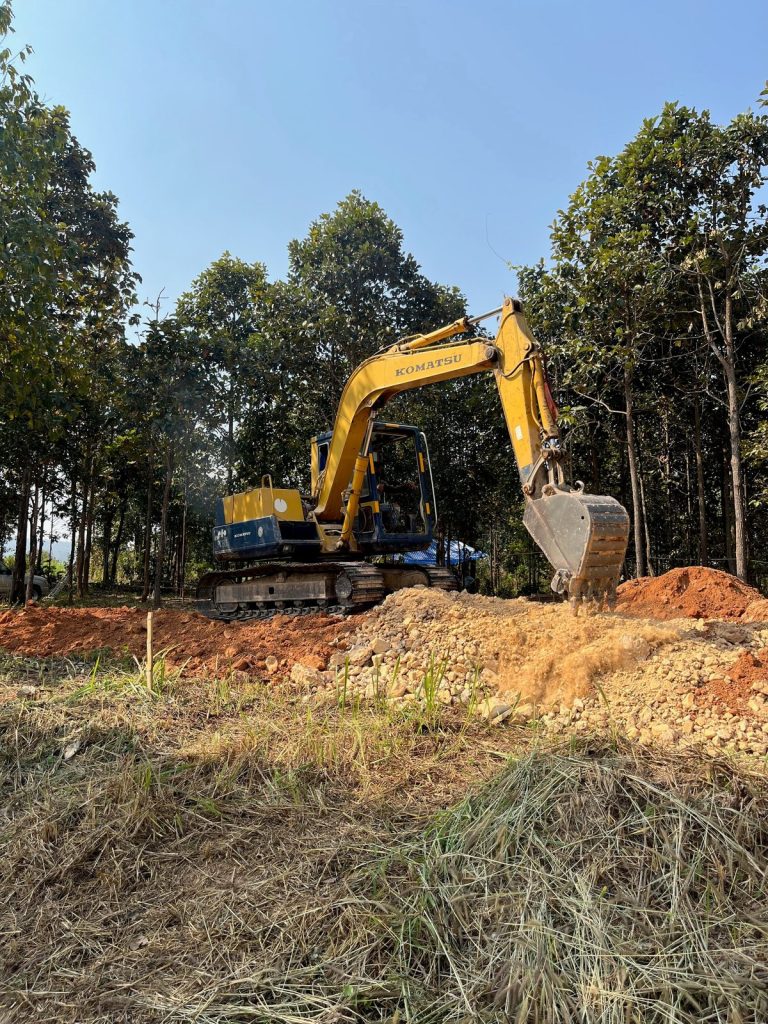 A Komatsu excavator shaping soil during land development among young trees at Sunshine Permaculture, Mae Taeng, Chiang Mai.