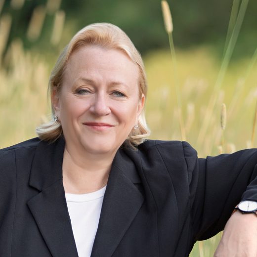 Catherine Austin Fitts, publisher of The Solari Report, in a black blazer standing in a grassy field.