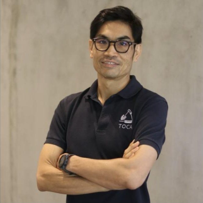 Arrut Navaraj, arms folded, in a navy TOCA polo shirt against a concrete wall.