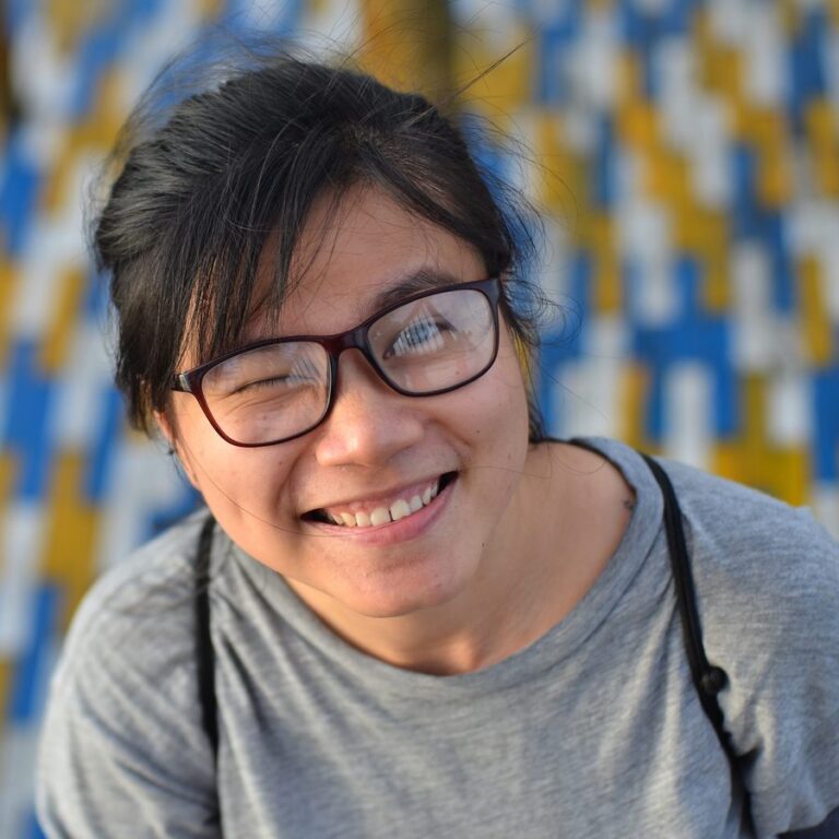Thao Kin of the Global Ecovillage Network Oceania and Asia, smiling at the camera in glasses and a grey top.