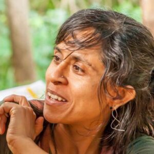 Trudy Juriansz of Permaculture for Refugees in conversation outdoors, mid-smile, with trees behind her.
