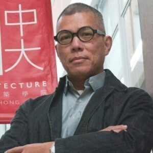 Edward Ng in round dark-framed glasses and a dark jacket, arms crossed, beside a red CUHK School of Architecture banner.