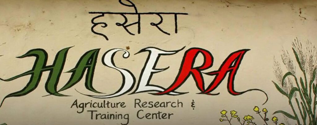 Hand-painted HASERA Agriculture Research and Training Center sign in Devanagari and English lettering, with drawn wheat and flowers at the right edge.