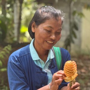 Natha Chaiphet in a blue denim jacket, smiling as she looks at an orange fire torch ginger flower in her hands.
