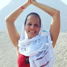 Sandra Lezama smiling with her hands raised above her head, wearing a white scarf, with a pyramid behind.