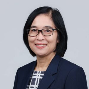 Warunee Ariyawiriyanan, smiling in glasses and a navy blazer, against a plain grey background.