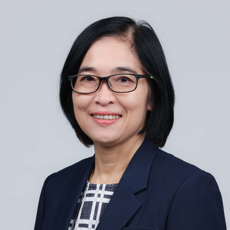 Warunee Ariyawiriyanan, smiling in glasses and a navy blazer, against a plain grey background.